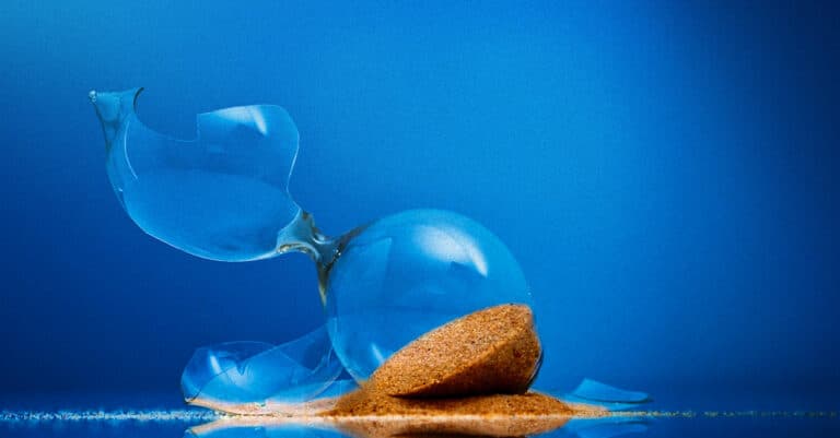 Blue glass ornament shattered into pieces with a small pile of sand on a blue background